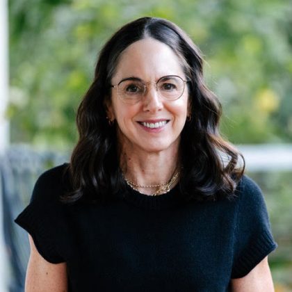 Dr Angela Lumsden smiles at the camera. She has dark medium length hair and is wearing a black short sleeve top.