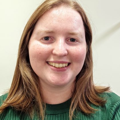 Dr. Lucy Smith smiles at the camera. She has ginger hair and is wearing a green sweater.